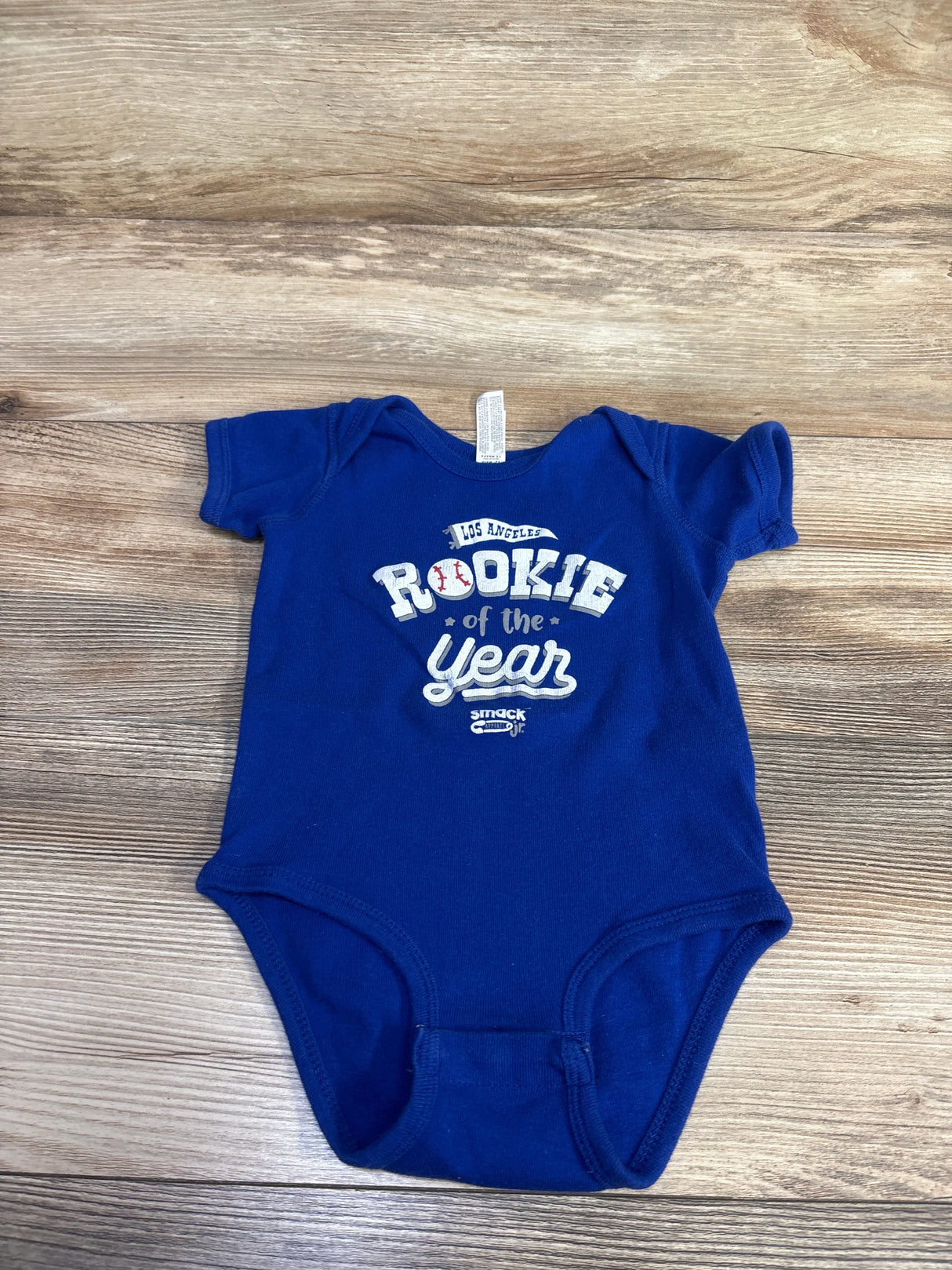 Top view of blue Rabbit Skins 12M bodysuit with Rookie of the Year front print and snap closures on wood background