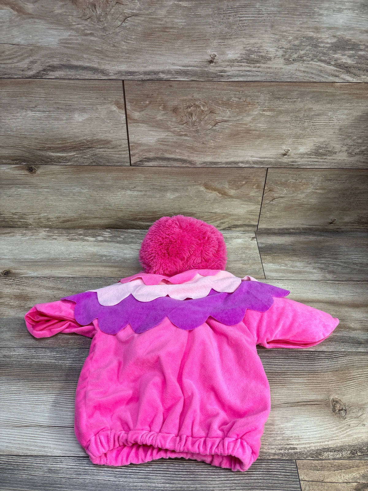 Rear view of pink plush flamingo costume showcasing fuzzy hood and purple scalloped collar on a wood floor