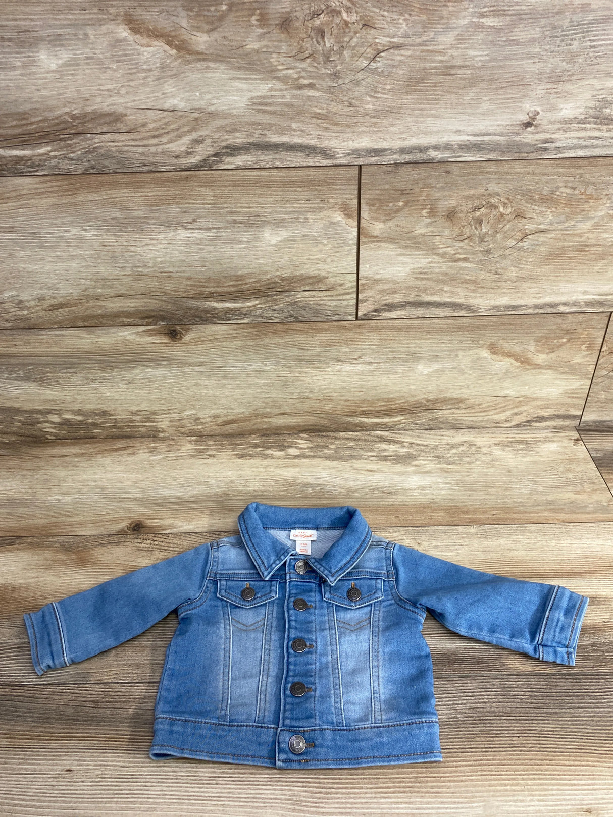 Light blue denim baby jacket with button closures and chest pockets on wooden background