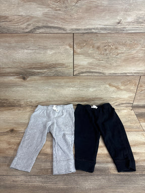 Flat lay of two Carter's baby pull-on pants, black and gray, showing elastic waist with white ties and cuffed legs on wood floor