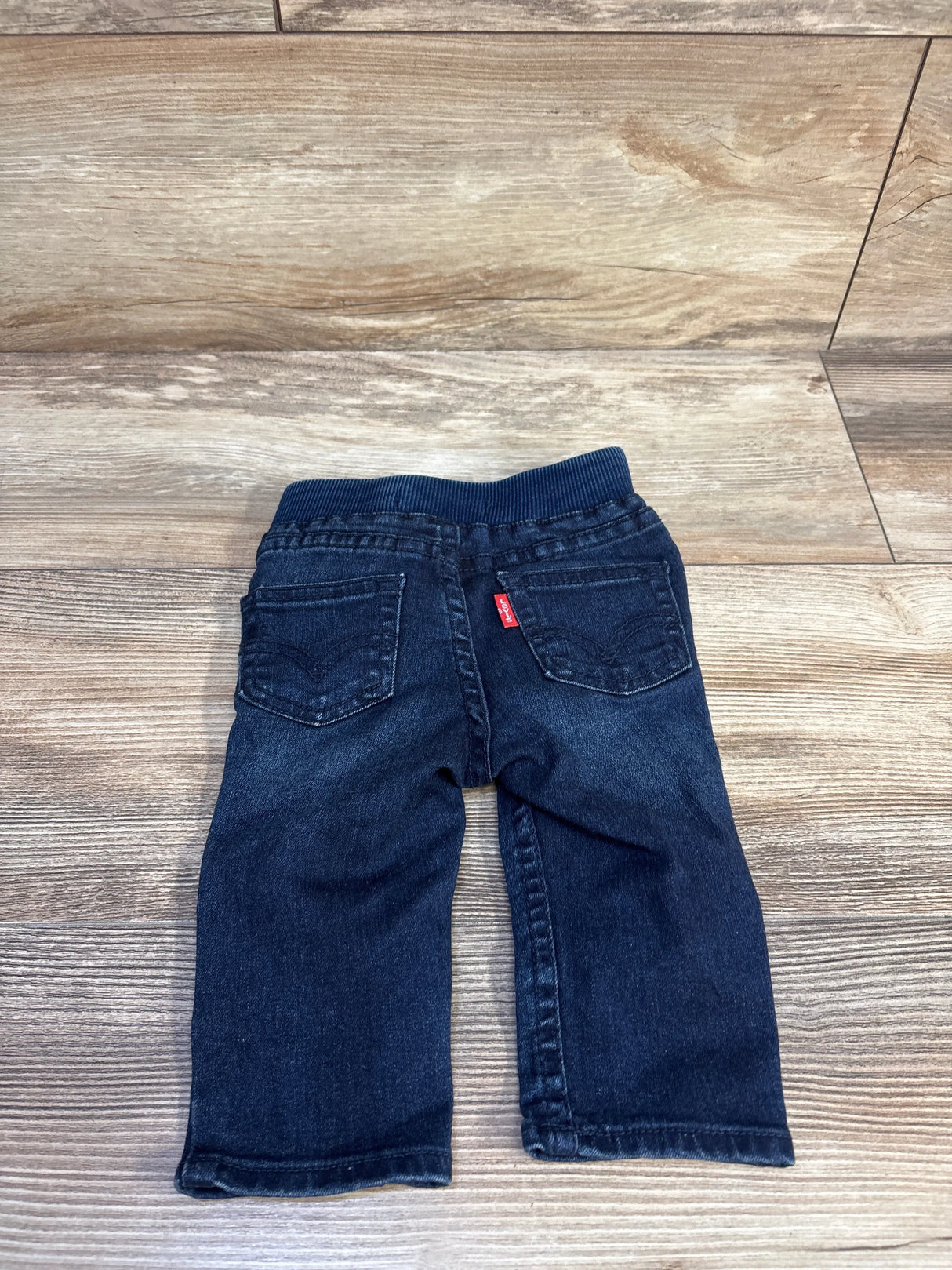 Back view of navy Levi's baby jeans, 6 months, showing ribbed elastic waistband, back pockets and red Levi's tab on wood background