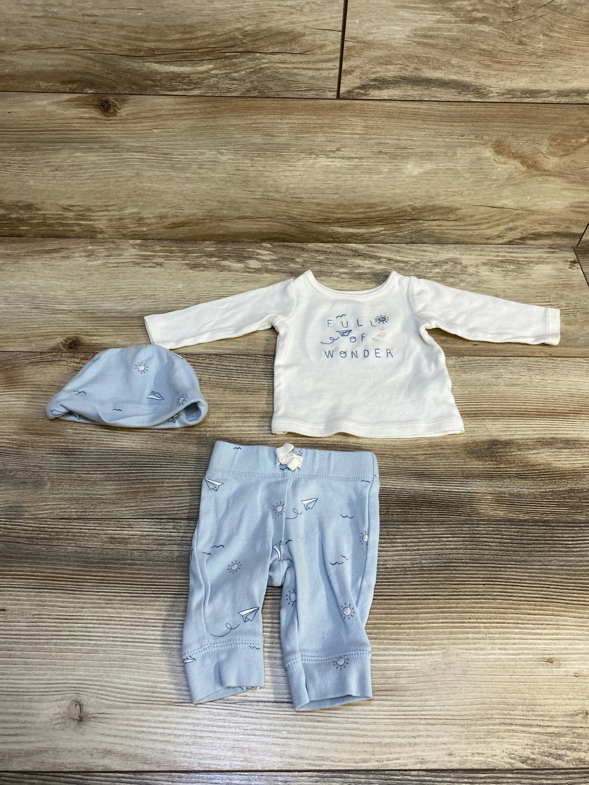 Baby boy outfit set with white long sleeve shirt, blue pants, and matching hat on wood floor
