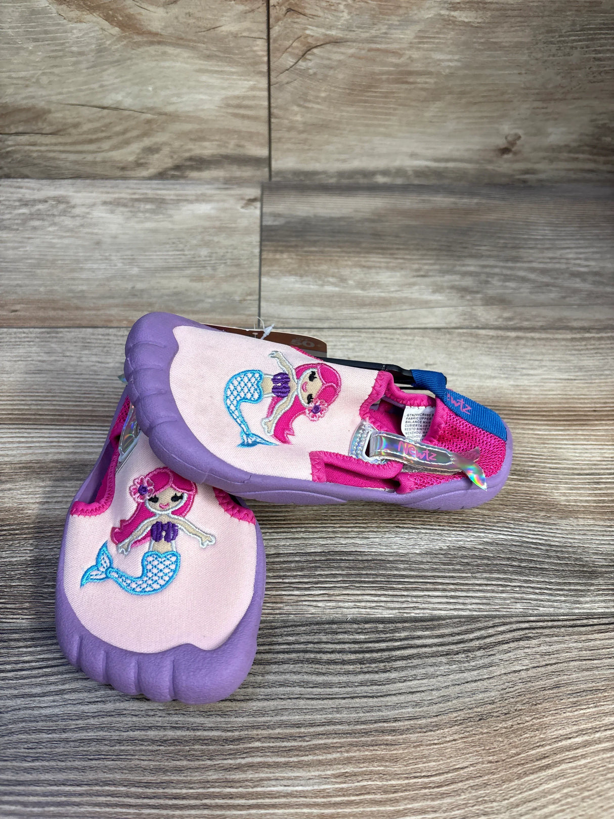 Three-quarter view of Newtz mermaid water shoes in purple and pink with embroidered mermaid and rubber toe on wood background