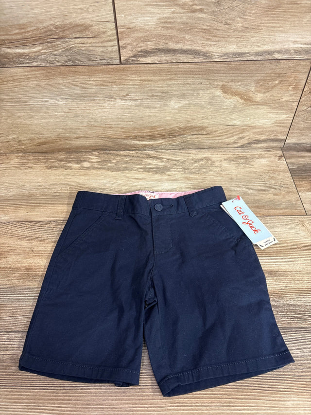 Front flat lay of Cat and Jack navy 5T school shorts showing button waist, side pockets, and pink inner waistband on wood floor