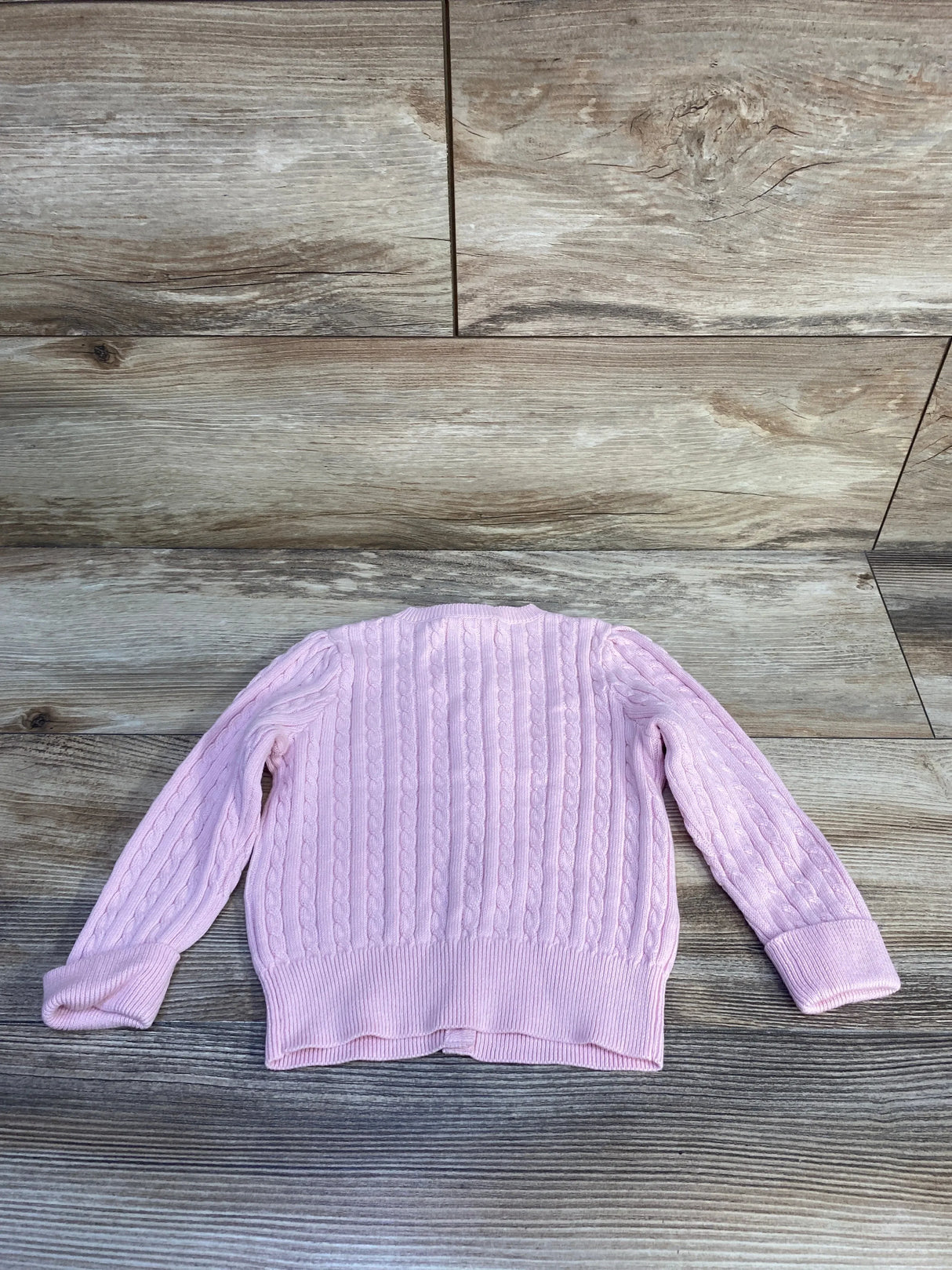 Back view of Ralph Lauren mini cable-knit cardigan in light pink showing cable stitch and ribbed hem and cuffs on wood floor