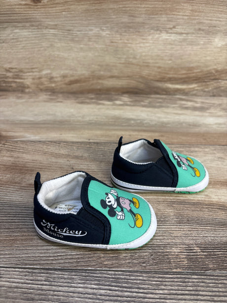 Baby slip-on shoes with Mickey Mouse design, mint green and black, on wood background
