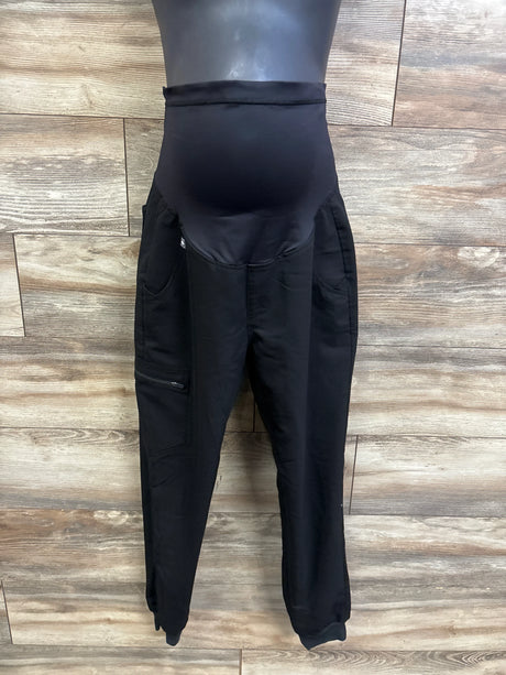 Front view of FIGS maternity scrub pants with high-rise belly panel, zip cargo pocket, and elastic ankle cuffs on wood background