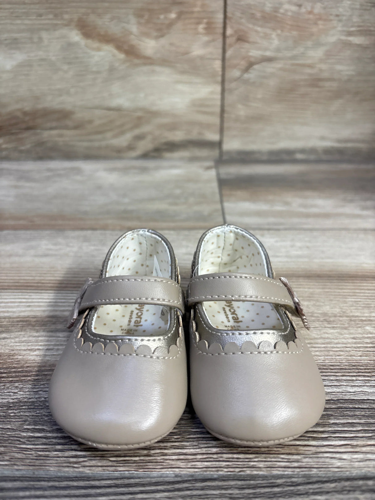 Front view of Mayoral Mary Jane Hojaldre tan baby shoes showcasing scalloped trim, hook-and-loop strap, and polka-dot lining on wood background