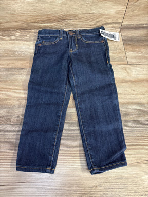 Dark blue kids jeans with front pockets and a tag, laid flat on wooden floor