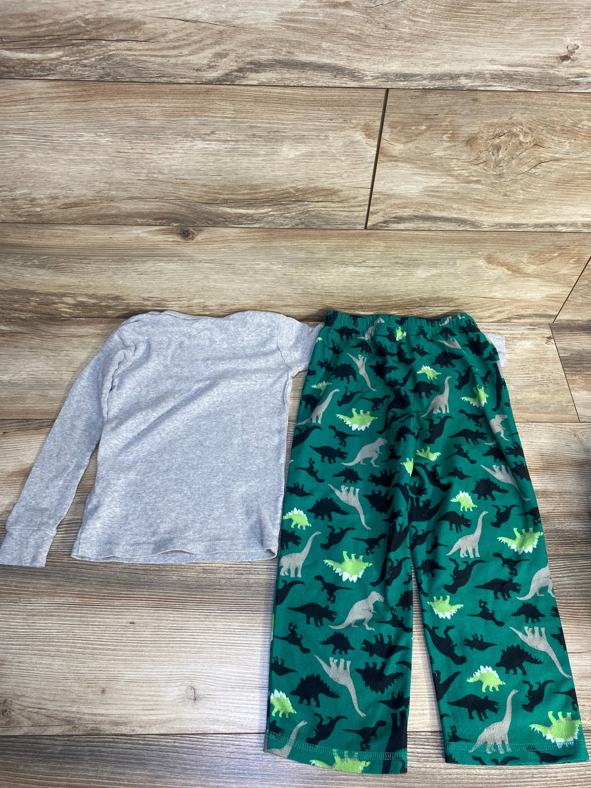 Kids long sleeve gray shirt and green dinosaur print pajama pants on wood background