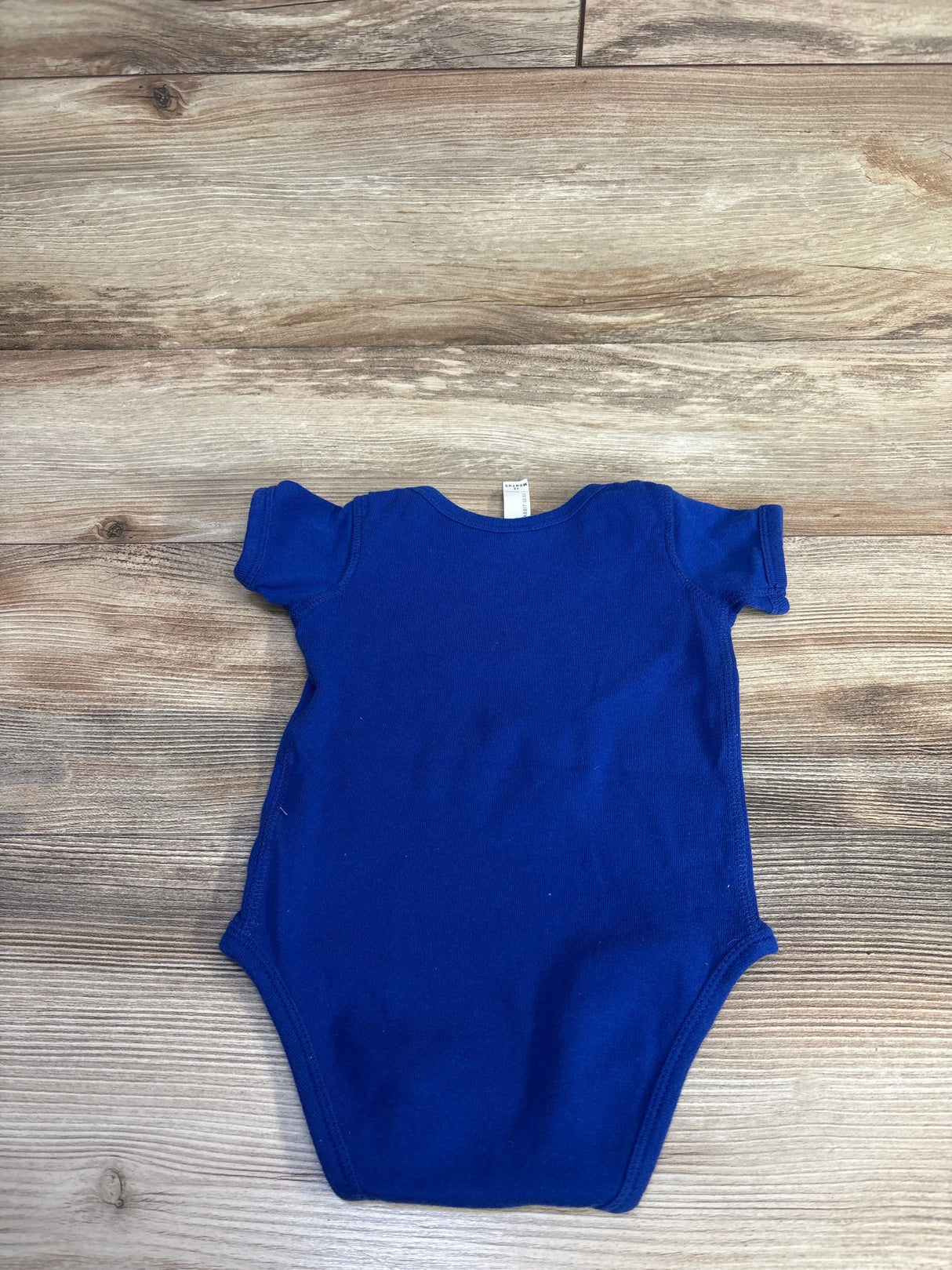 Flat-lay back view of blue Rabbit Skins Rookie of the Year 12m bodysuit with short sleeves on wood background