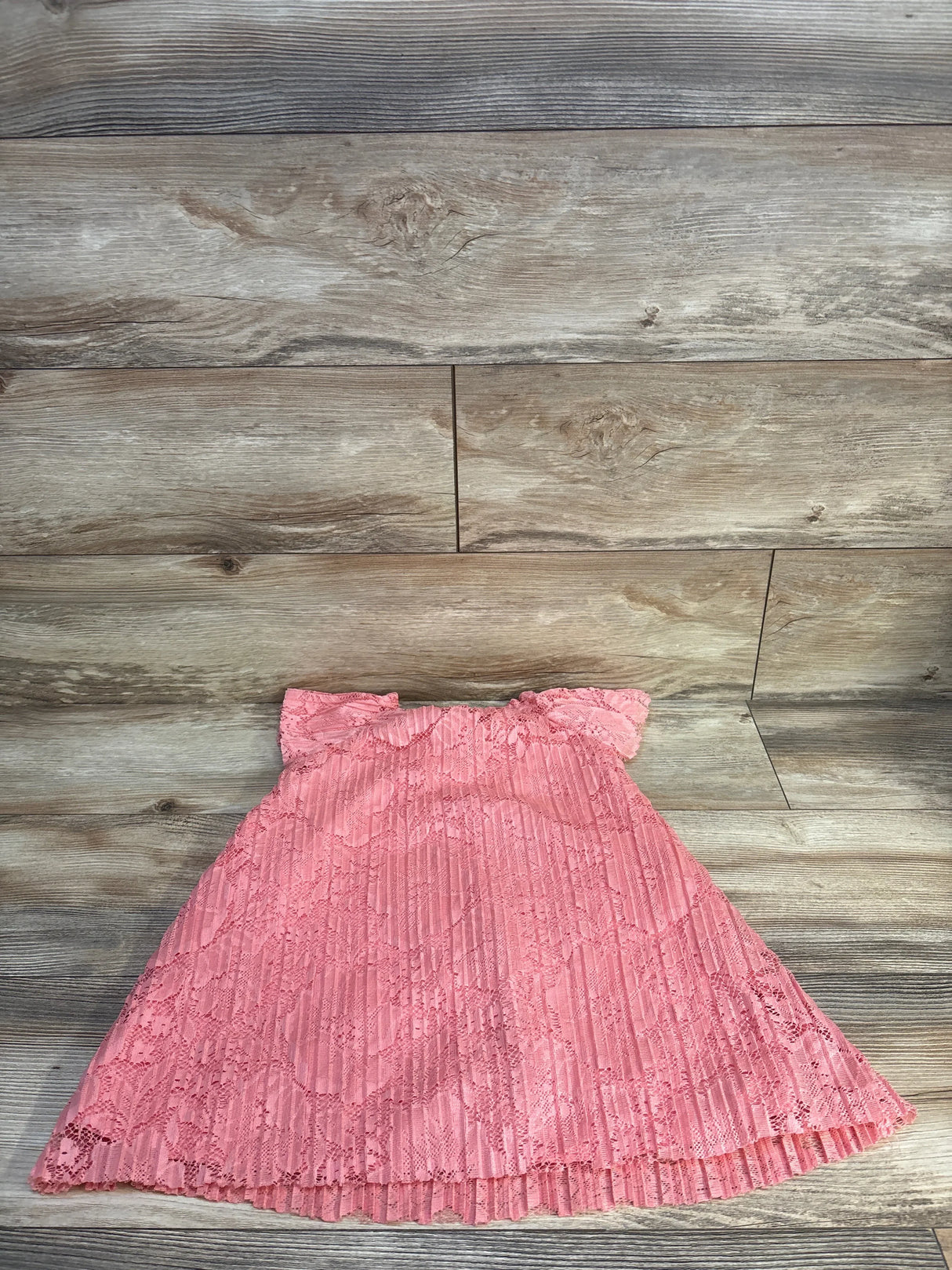 Pink lace baby dress with ruffled sleeves and pleated skirt on wood floor