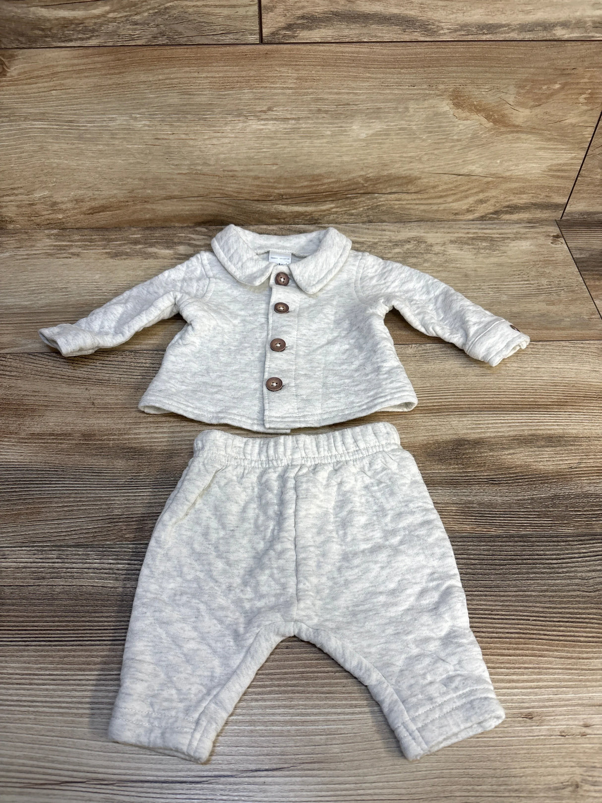 Light grey baby outfit with button-up jacket and matching pants on wood background