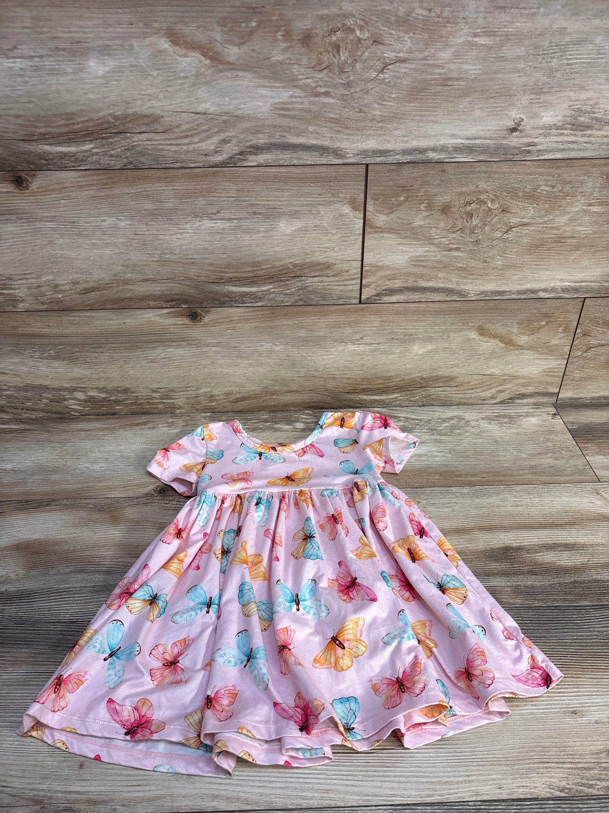 Flat lay of pink Mila and Rose twirl dress showcasing multicolored butterfly print and short puff sleeves on wood background