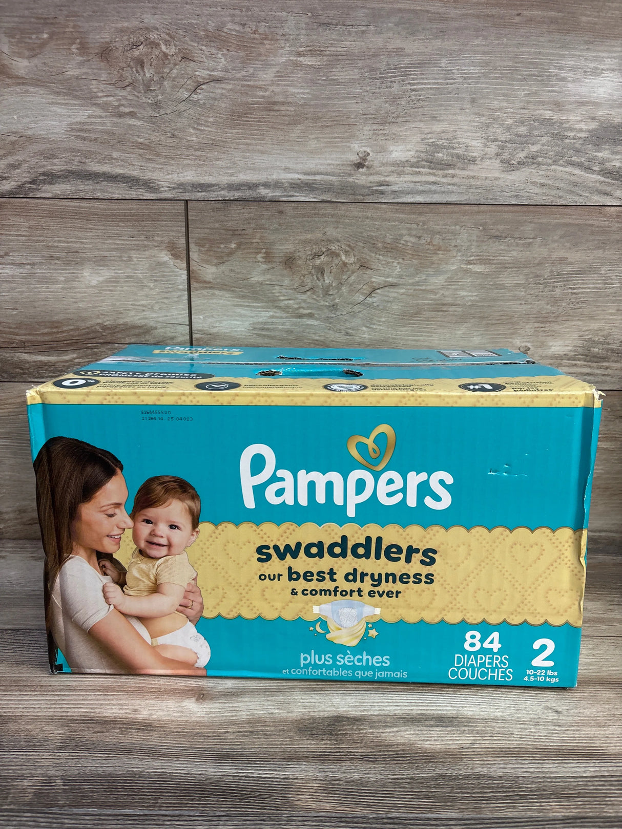 Front view of Pampers Swaddlers diaper box, Size 2 (10–22 lbs), 84 count, shows mother holding baby and 'our best dryness' text on wood background