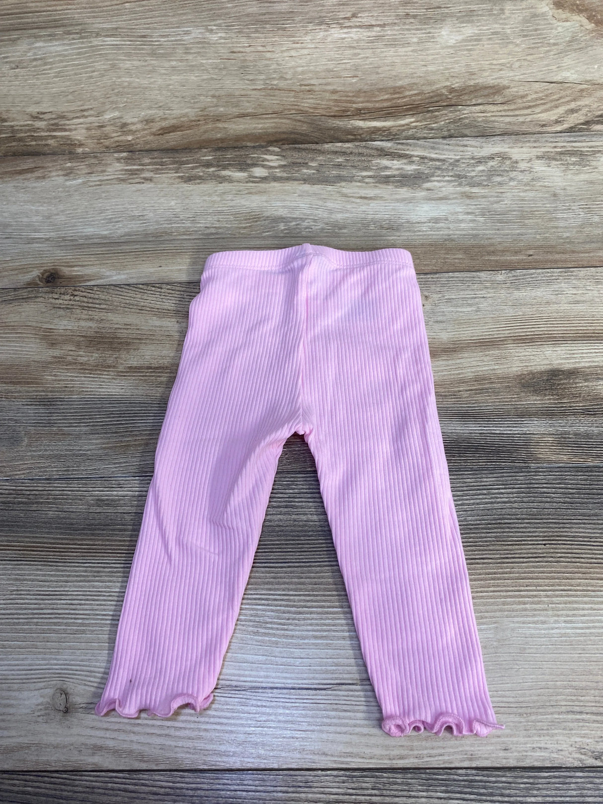 Flat lay of girls' Old Navy pink ribbed leggings showing ribbed texture and ruffled hems on wood background
