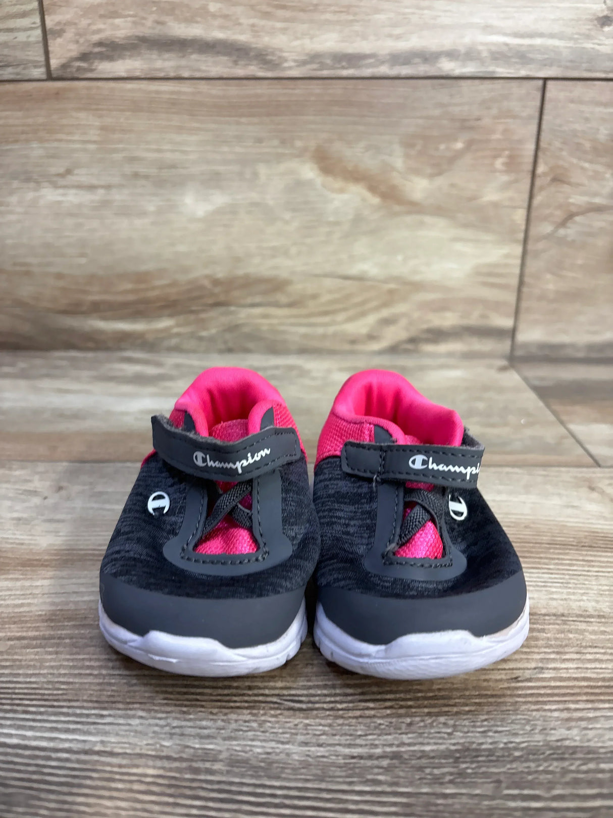 Front view of Champion Gusto toddler sneakers in grey and pink showing velcro strap, cushioned pink lining, and white rubber sole on wooden floor
