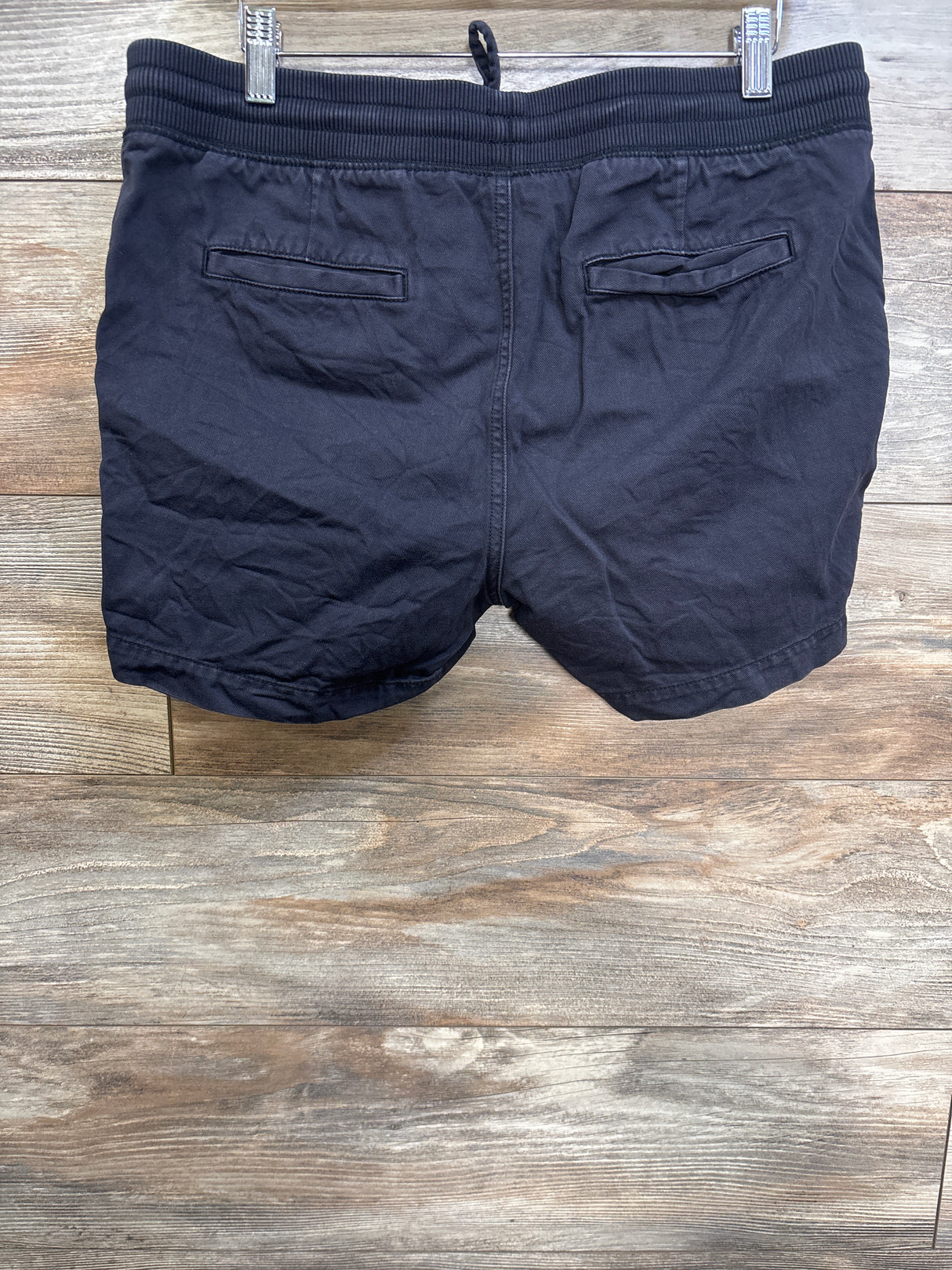 Back view of black Gap maternity shorts with ribbed elastic waistband, drawstring loop and back welt pockets on wood background