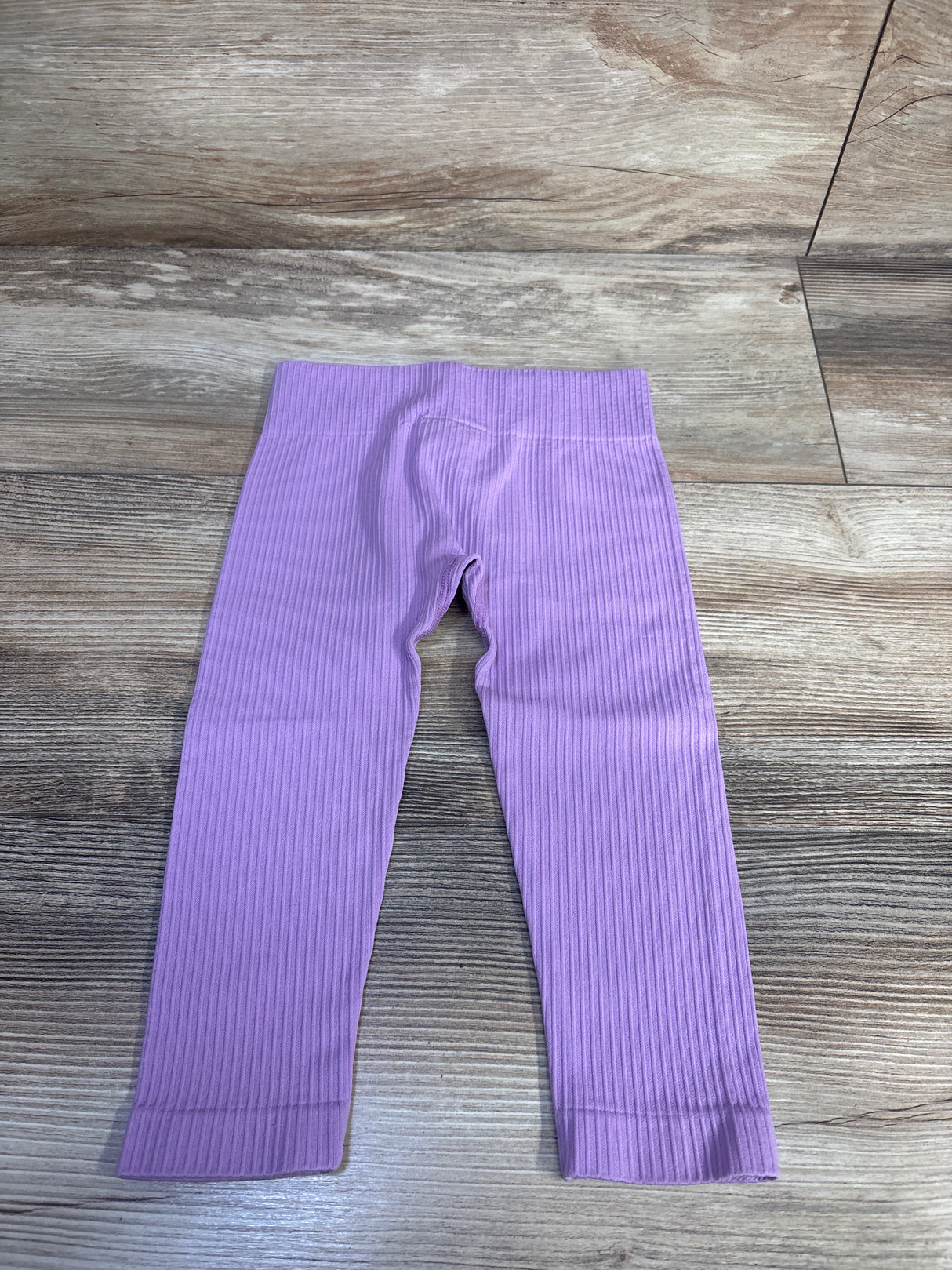 Flat lay of lilac toddler ribbed leggings (12–24 months) showing ribbed texture and elastic waistband on wood floor background