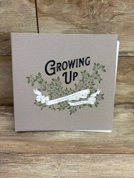 Front cover of Growing Up memory book showing leafy branches and ribbon design on a beige background