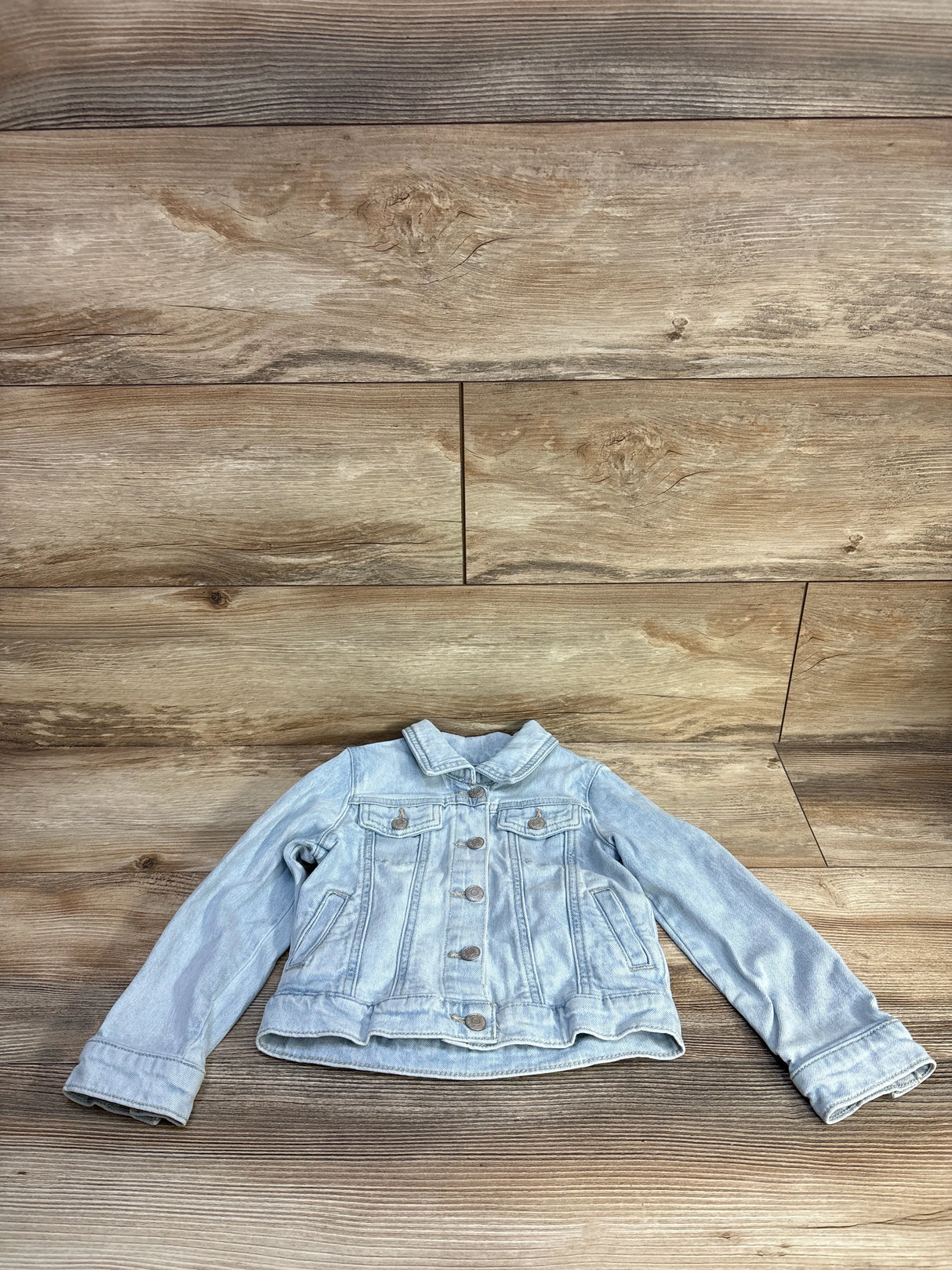 Front flat-lay of light blue Cat & Jack denim jacket 4T showing button-front and chest pockets on wood background