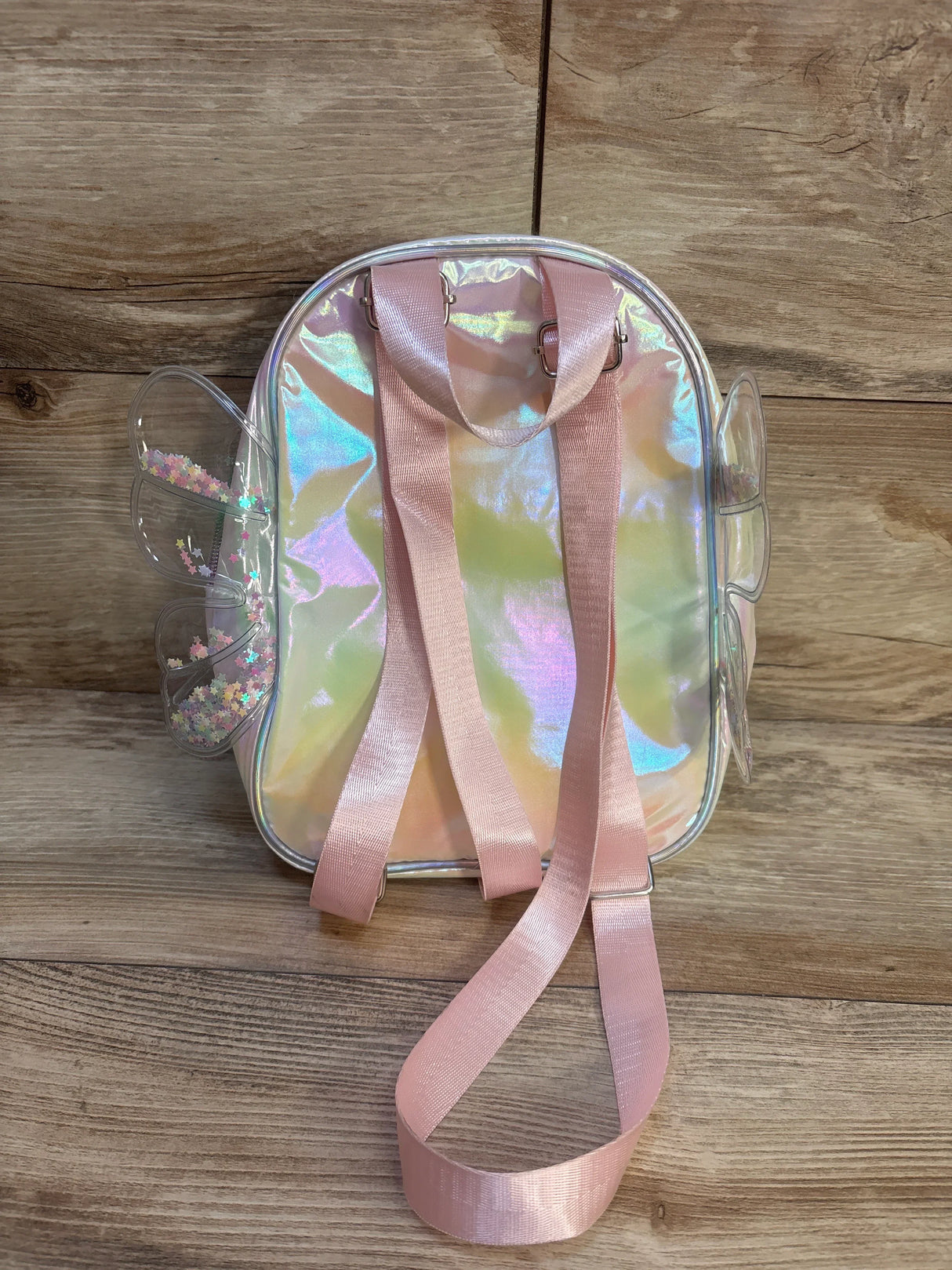 Iridescent kids backpack with pink straps and butterfly wing accents on wood floor