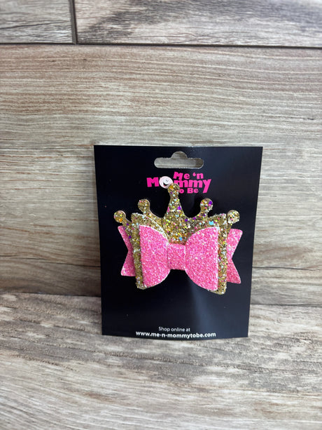 Front view of layered crown glitter hair bow in pink and gold on black display card with wood background