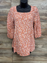 Front view of orange maternity floral blouse showing square neckline, ruched three-quarter sleeves and white-red floral print on wood background