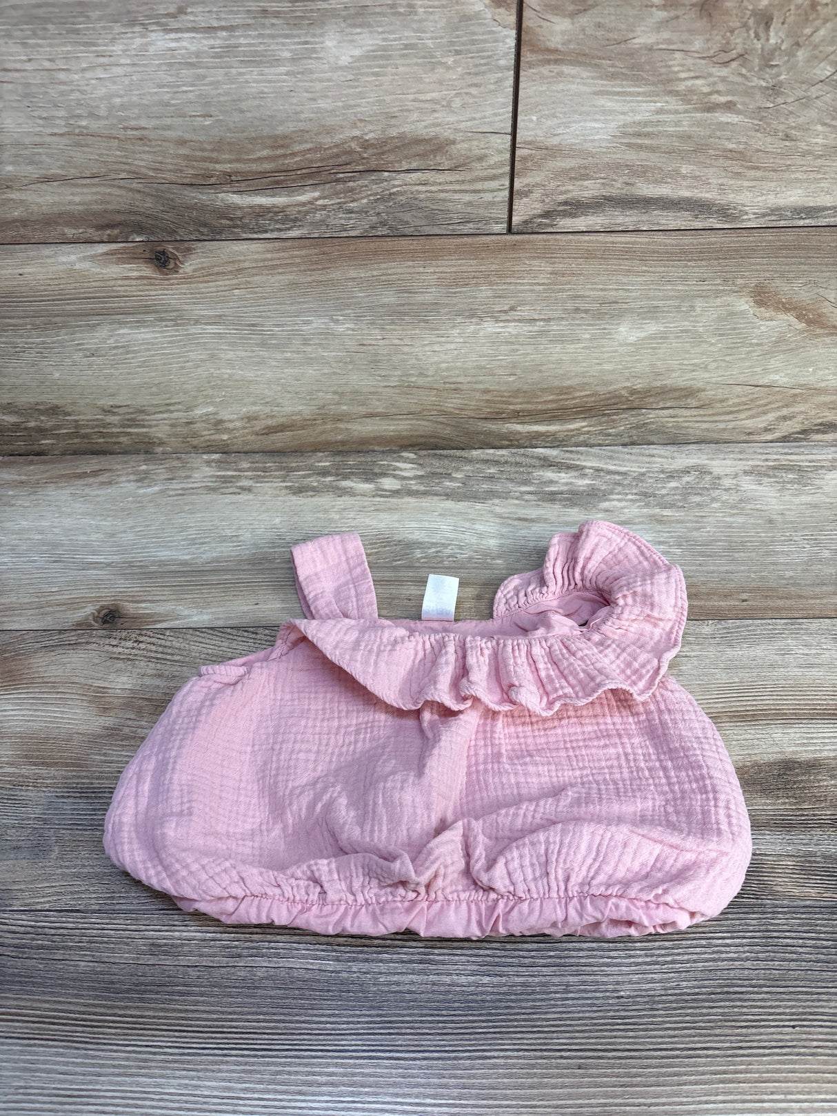 Flat lay of pink gauze toddler top (3T) showing ruffled neckline, single shoulder strap, and elasticized hem on wood background