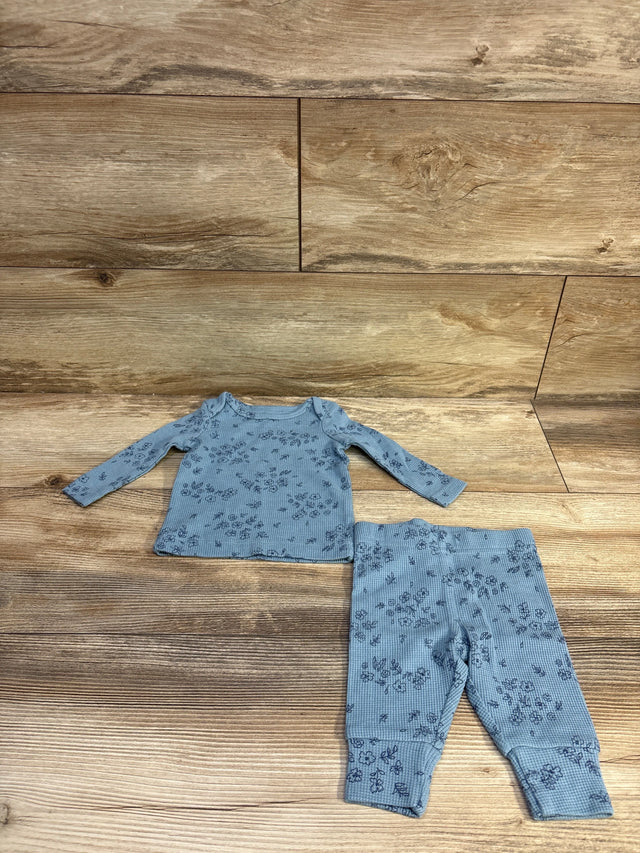 Top-down view of a blue two-piece waffle knit shirt and pants set with floral pattern, laid flat on a wood-grain background