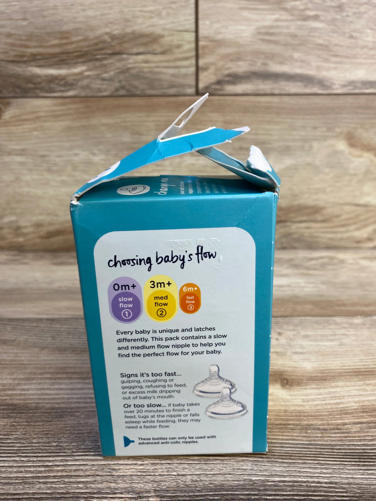 Side view of new Tommee Tippee Advanced Anti Colic 5oz bottle box with Choosing Babys Flow nipple flow guide and torn opening on wood plank floor