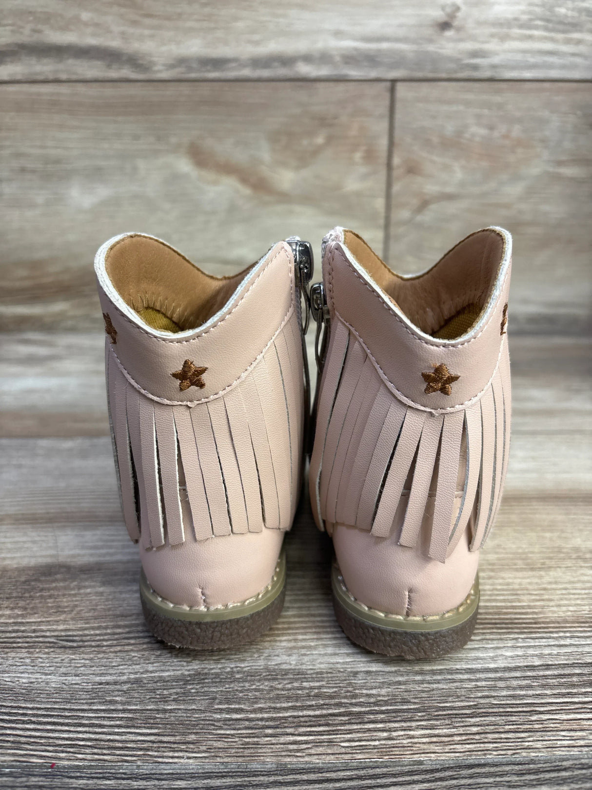 Rear view of pink toddler cowgirl boots showing fringe and embroidered star detail on wood plank background