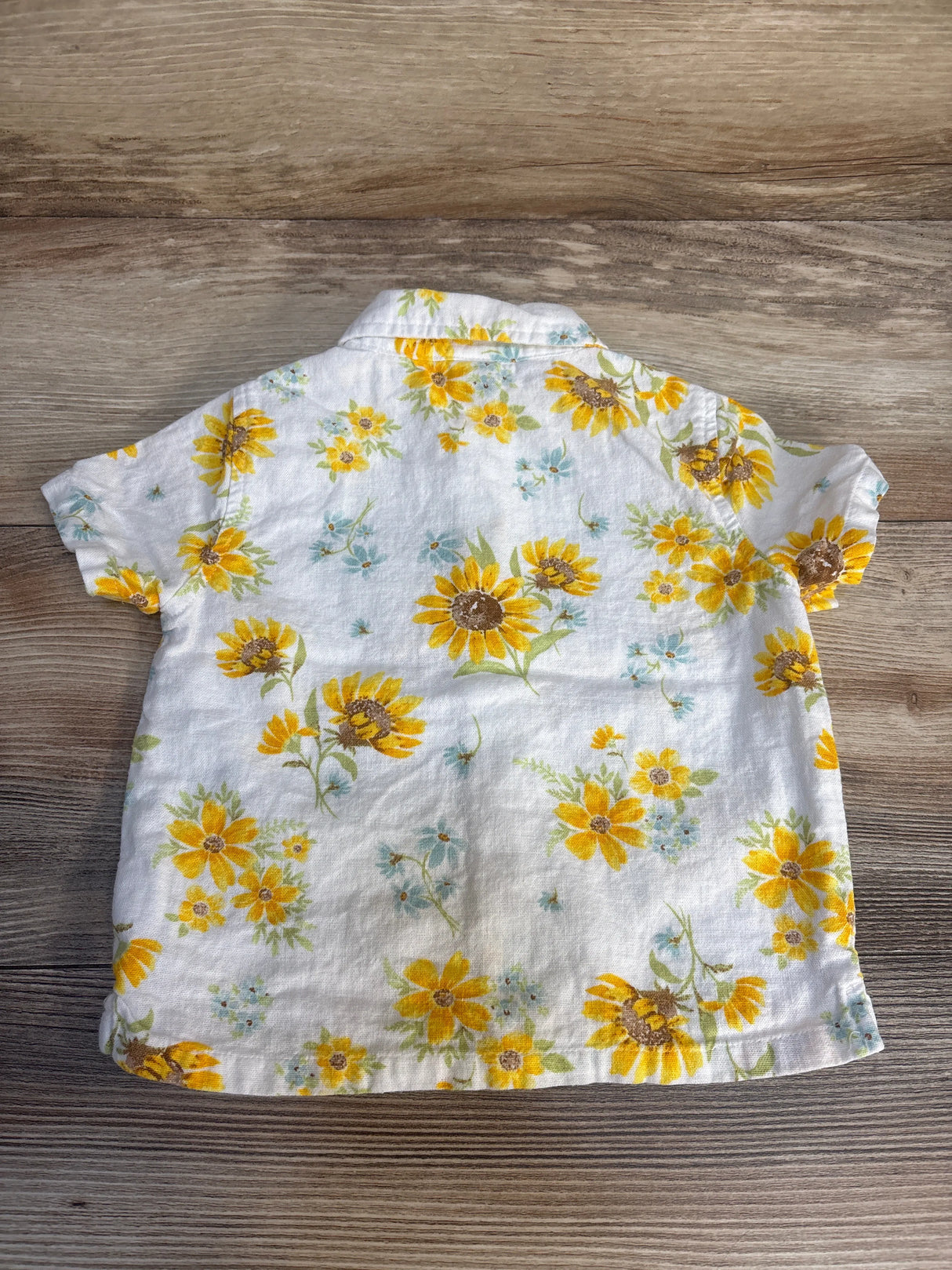 White short sleeve toddler shirt with yellow sunflower print, back view on wood surface.