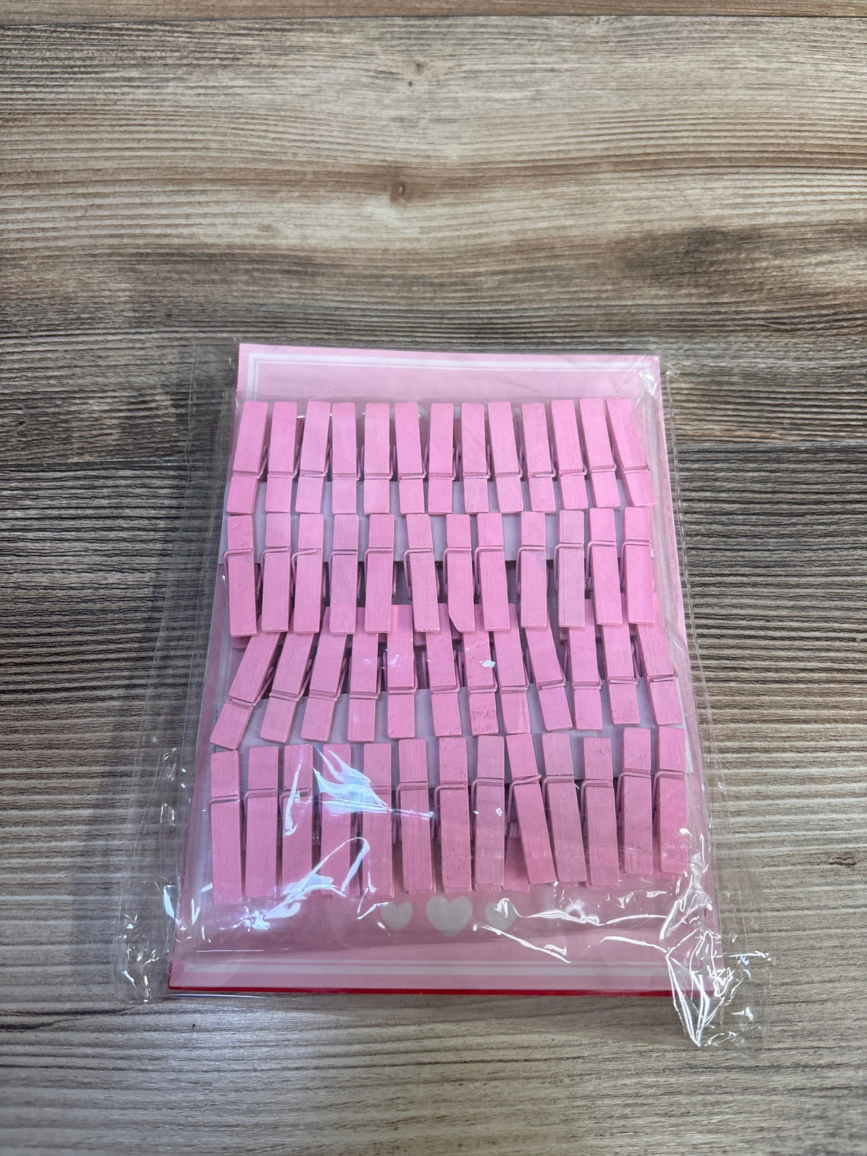 Top-down view of pink wooden clothespins for the Don't Say Baby shower game on pink backing card in clear plastic