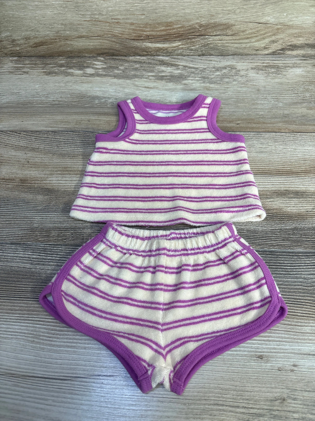 Top-down flat lay of newborn terry cloth tank top and shorts showcasing ivory with purple stripes and trim on wood background