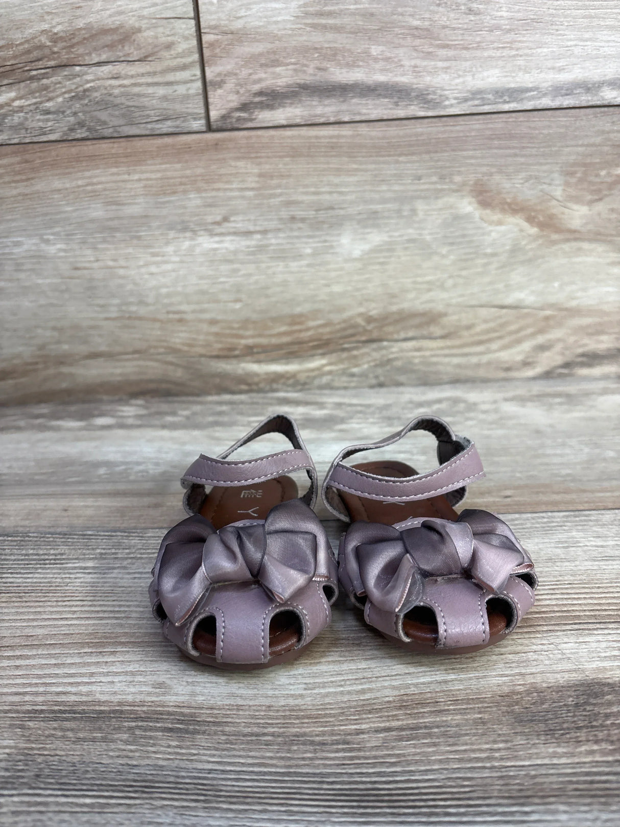 Front view of EYY mauve toddler sandals showcasing knotted bows, open-toe cutouts and ankle straps on light wood background