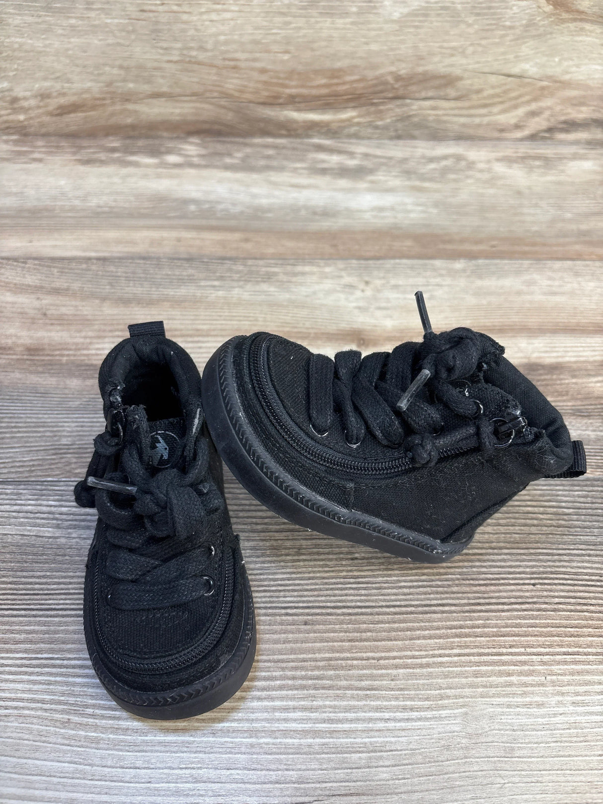 Top view of Billy Footwear adaptive high top sneakers size 5c in all black with side zipper closure and laces on wood plank background