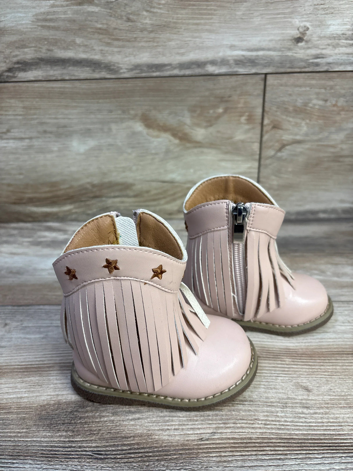 Three-quarter view of pink toddler round-toe cowgirl boots showing fringe, star accents and side zipper on wood background