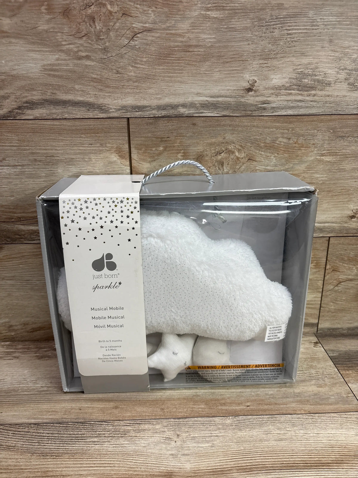 Front view of Just Born musical mobile showcasing sparkly gray stars in clear packaging on a wood surface