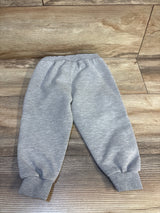 Gray kids sweatpants with elastic waist and cuffs, laid flat on wood floor