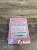 Top-down view of Don't Say Baby shower game set with pink 5x7 sign and 50 pink clothespins in plastic packaging on wood table