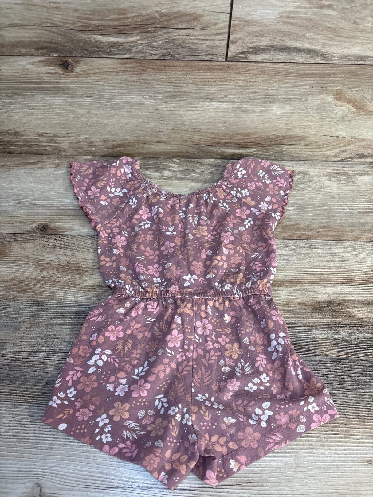 Flat lay of Lucky Penny mauve floral shortie romper size 4T showcasing ruffled sleeves and elastic waist on wood floor