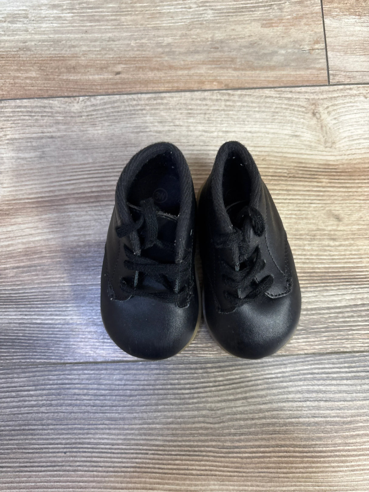 Top-down view of Teeny Toes Oxford first-walker shoes in black showcasing lace-up front and rounded toes on light wood floor