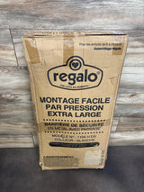 Front view of boxed Regalo extra tall metal baby gate in white showing packaging label on wood panel backdrop