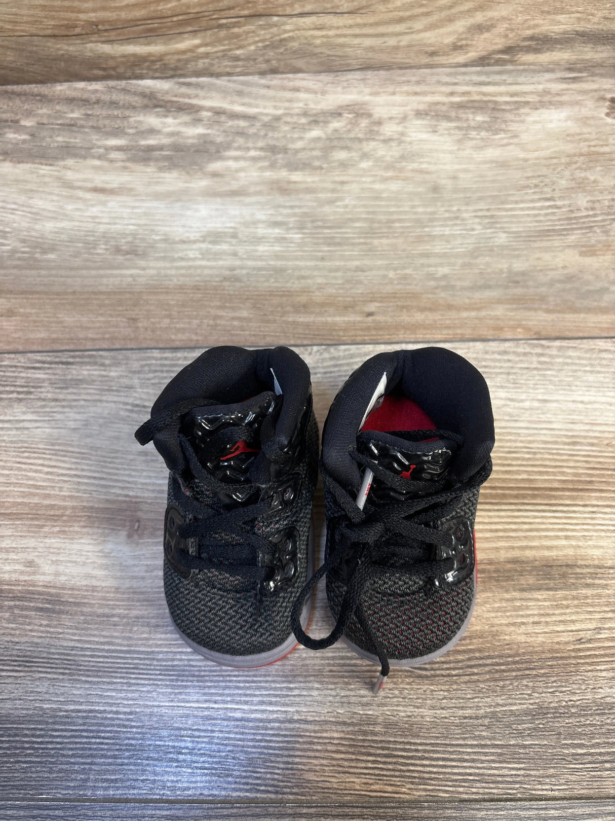 Black and red toddler sneakers with mesh fabric and velcro straps on wood floor