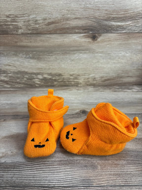 Orange baby booties with black jack-o'-lantern faces, Halloween themed on wood background