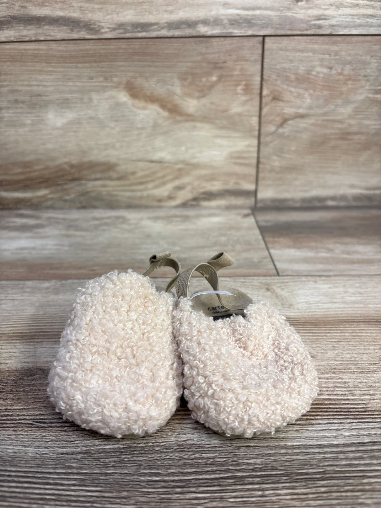 Front view of Child of Mine beige slip-on baby clogs showcasing plush boucle texture and elastic heel straps on wood plank background