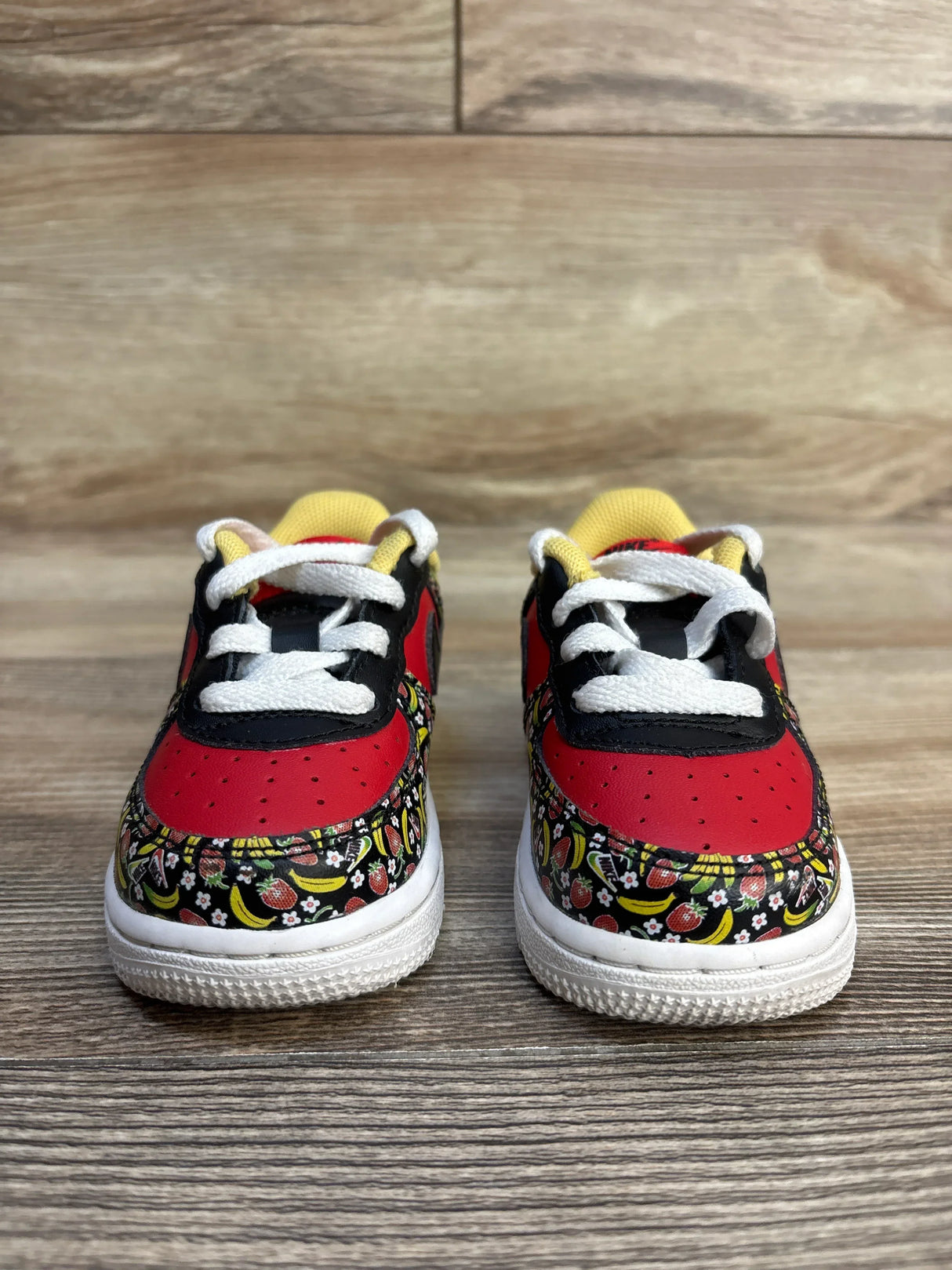 Kids' red and black sneakers with fruit print, white laces, yellow accents on wood floor