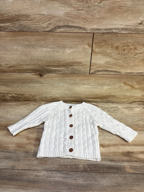White cable knit baby cardigan with brown buttons on a wooden background