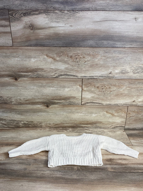 White knitted baby sweater laid flat on wooden floor background, kids clothing resale item